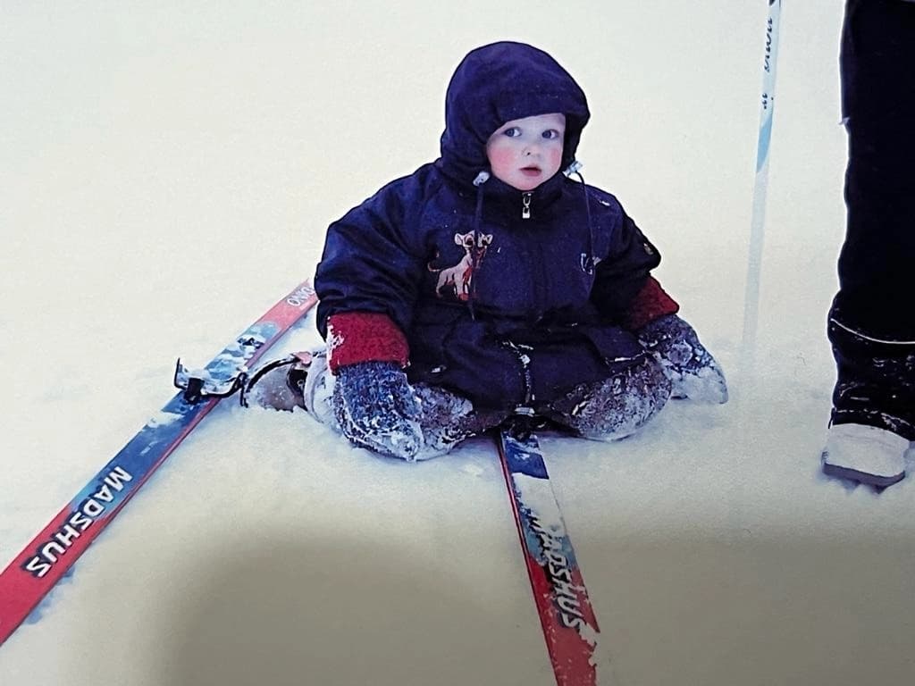 Toddler Dmitry sitting on skis in the snow
